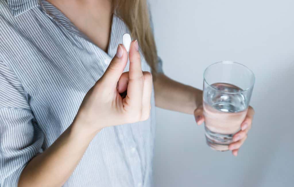 holding a white pill and a glass of water
