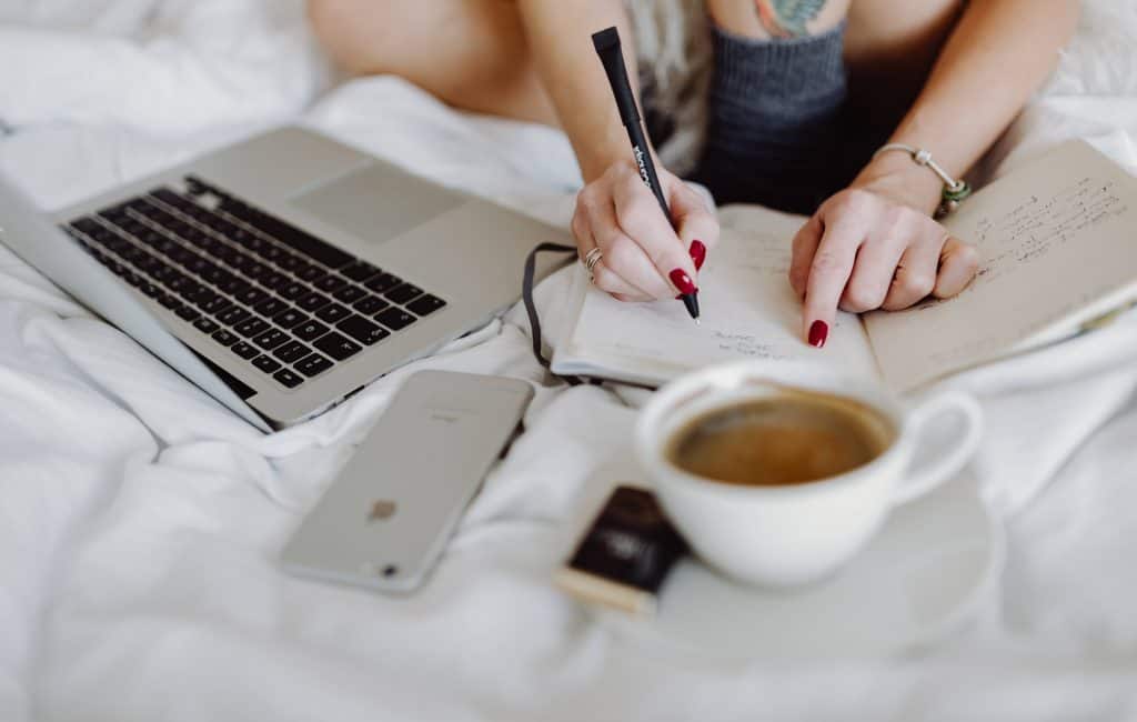 Woman working on a laptop while enjoying a breakfast coffee and chocolate in bed