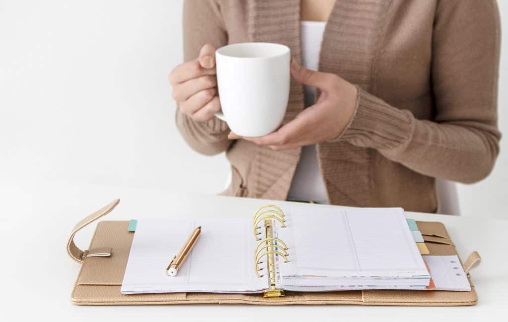 woman holding a white coffee mug next to her planner