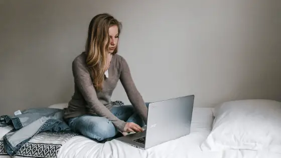 typing on her laptop while sitting on the bed