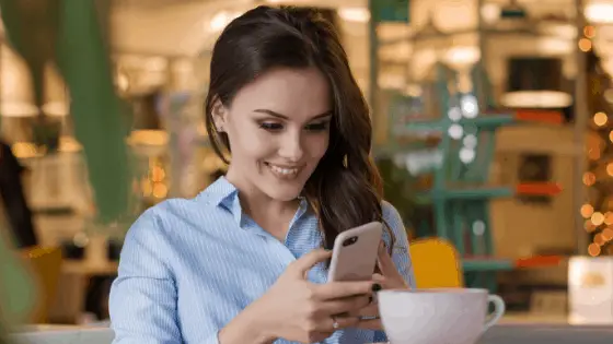 woman in a coffee shop smiling while using her phone