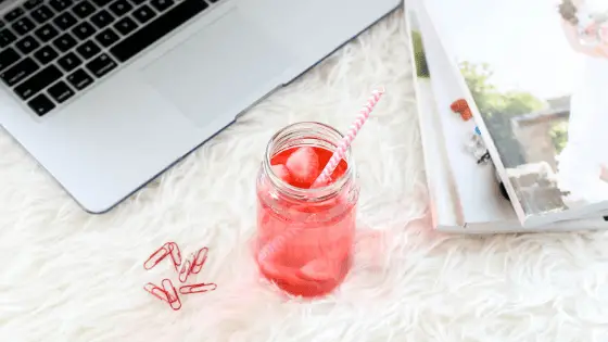 light red juice near red paper clips and magazines on a fluffy white carpet