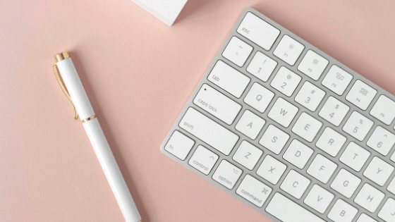 white keyboard and white ballpen against a pink background