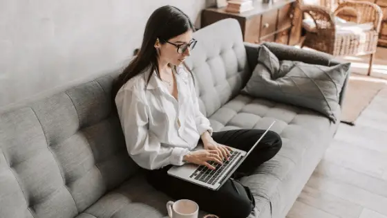 woman with eyeglass working in her laptop while sitting on a gray sofa