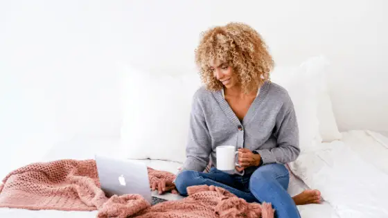 woman with blonde bushy curly hair sitting in bed working on her laptop