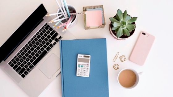 photo of mini calculator, macbook, and a blue notebook