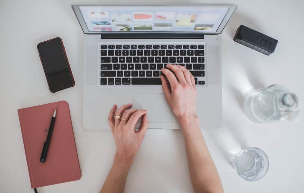 picture of a woman's hand on laptop next to a smart phone and a planner