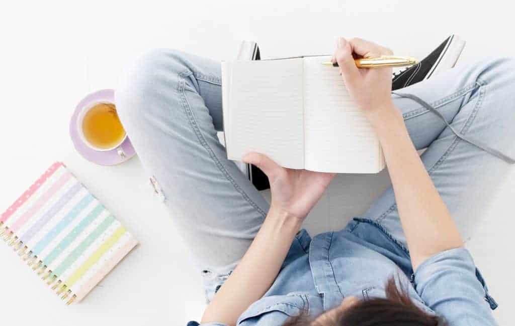 woman sitting on a floor writing on her journal