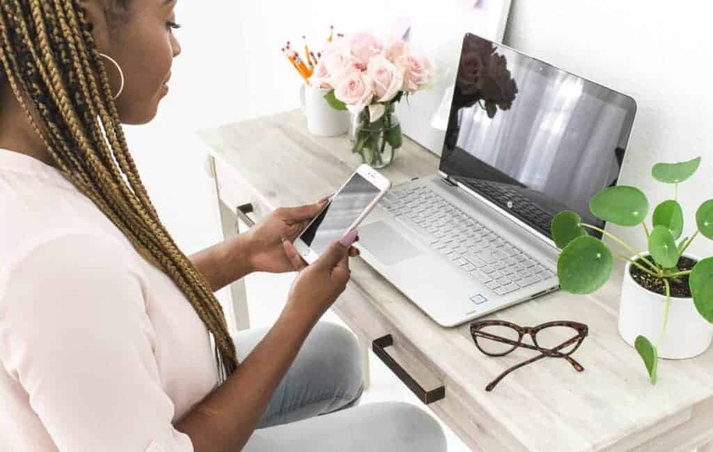 woman using her phone while sitting in front of her laptop