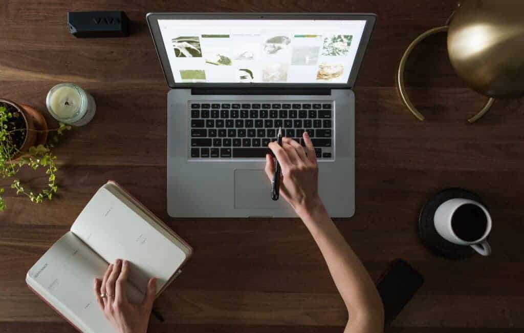 woman scrolling down through her laptop and taking notes