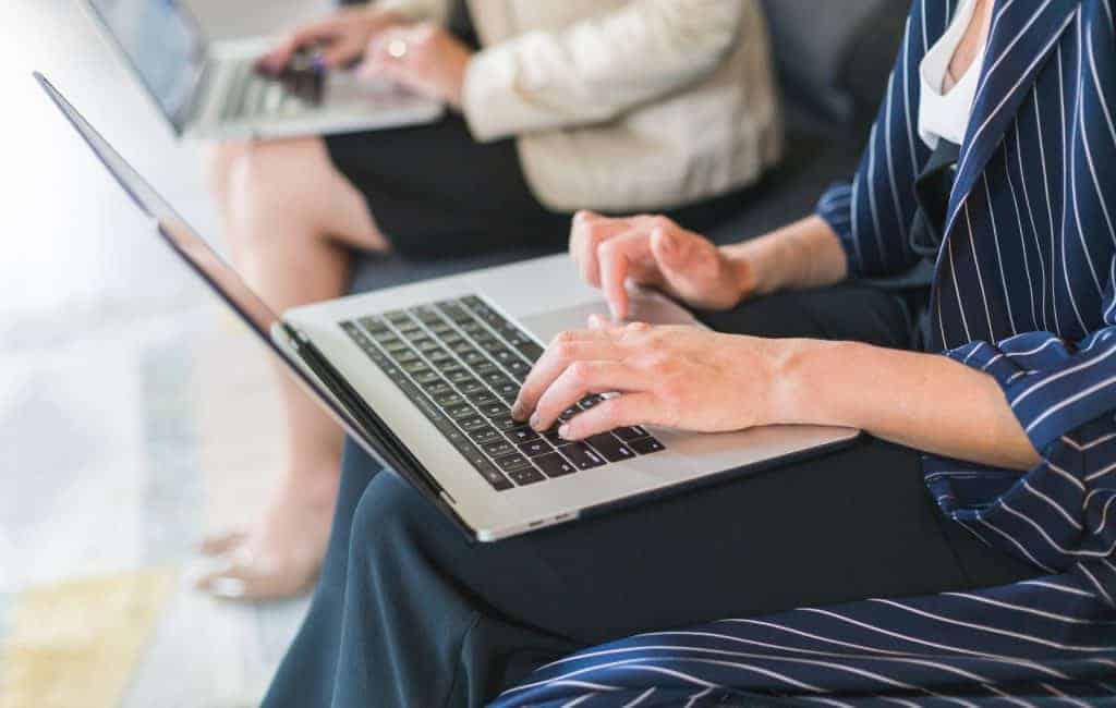 a photo of a woman sitting on a sofa working on her laptop next to a woman who's also working on a laptop