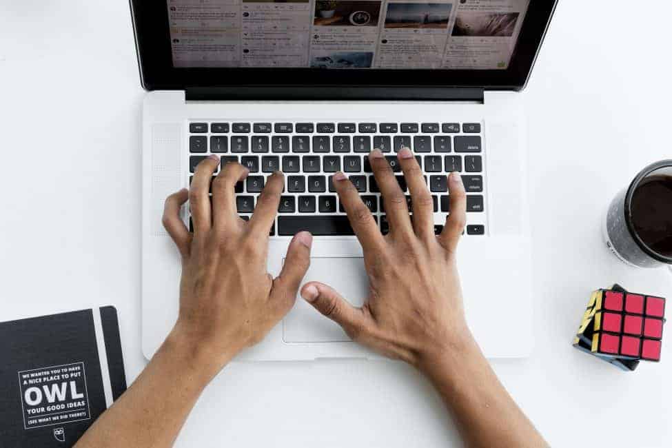 mans hand on keyboard computer next to rubik's cube