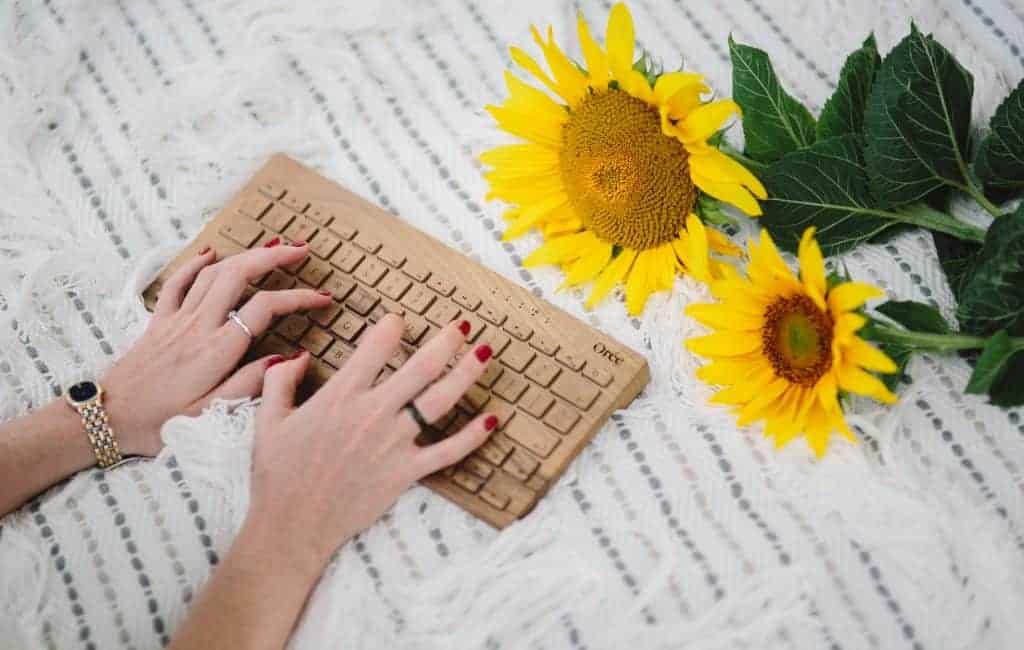 a woman's hand typing on a keyboard next to a sunflower