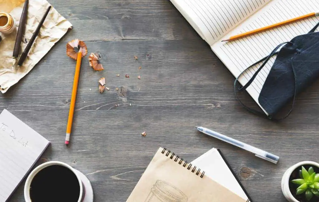 sharpened pencils, notebooks, blue pen and coffee on a wooden table