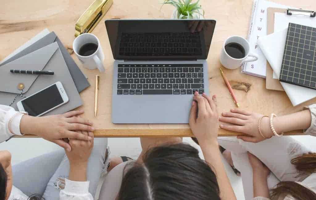 three woman sitting on a desk working together