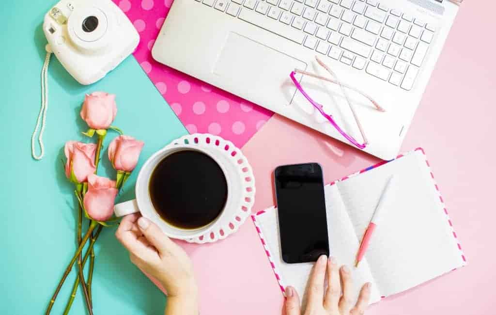 woman holding a coffee next to her phone and laptop