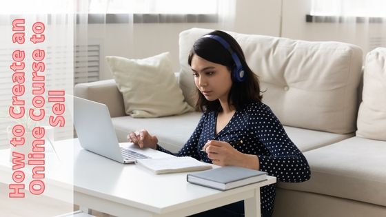 photo of a woman sitting on the floor in front to a low table with a laptop, notebook, glass of water and hardcover book on it.  She's looking into the laptop screen and she has headphones on and a pen in her hand